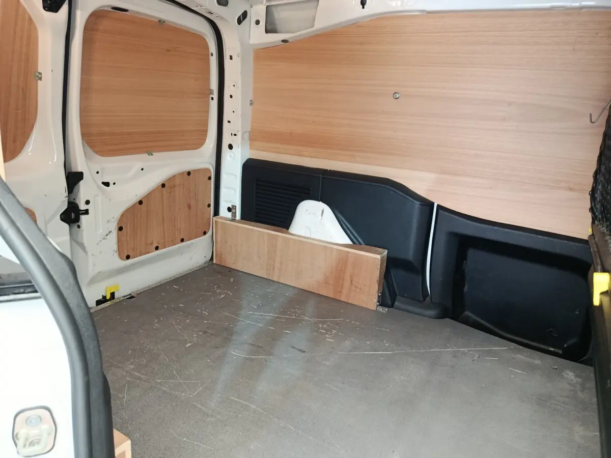 Vue intérieure arrière du Peugeot Partner blanc 2018, montrant l'espace de chargement avec cloison bois et protections latérales.