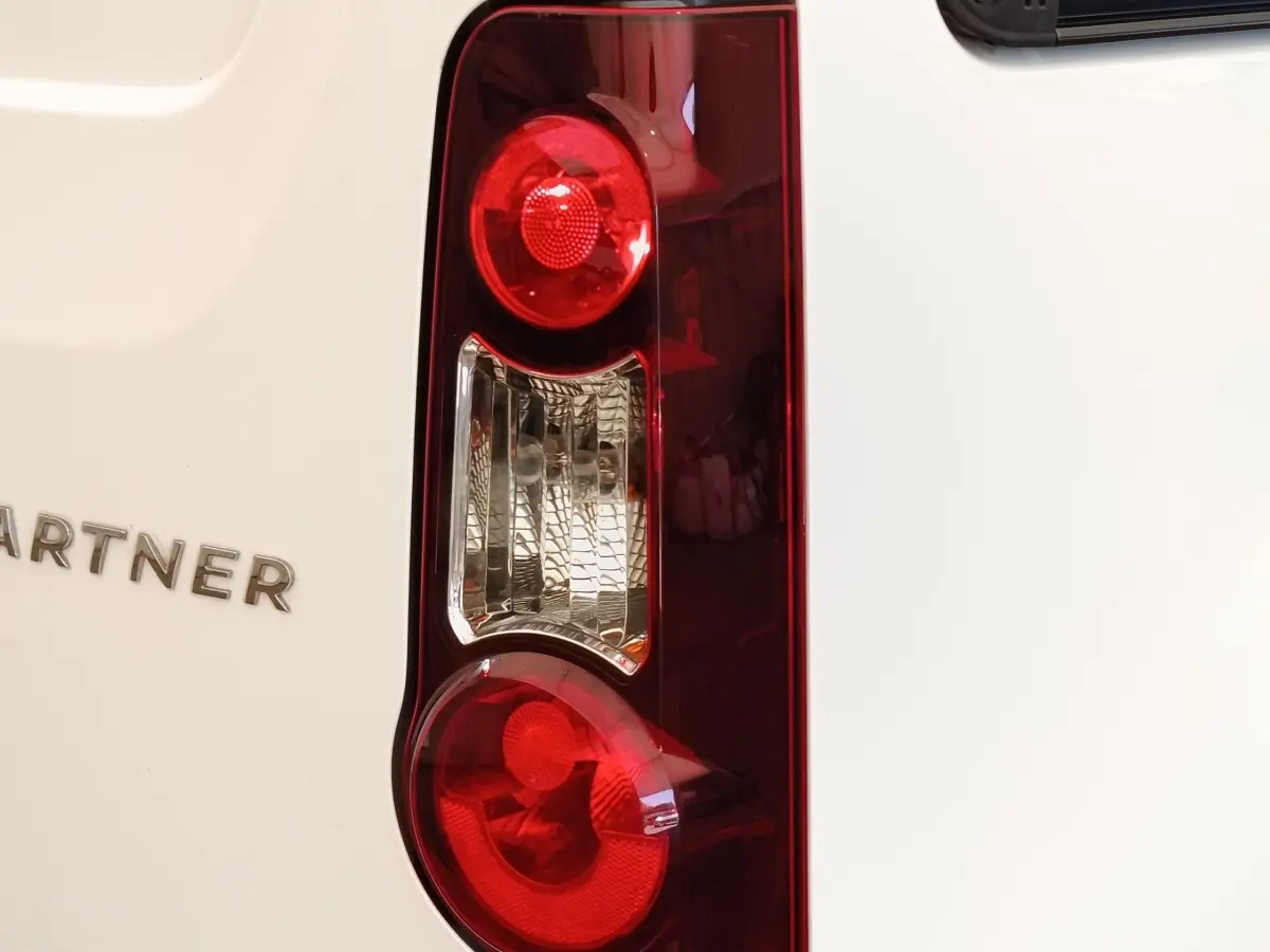 Gros plan sur le feu arrière droit rouge et blanc du Peugeot Partner blanc, avec le logo PARTNER visible sur la carrosserie.