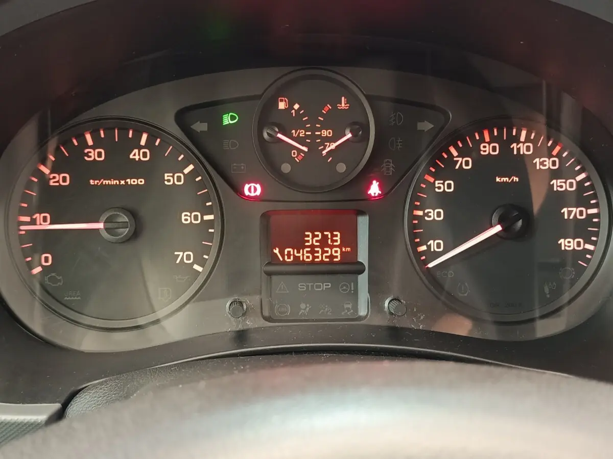Vue rapprochée du tableau de bord du Peugeot Partner blanc, affichant compteur et témoins lumineux rouges et verts.
