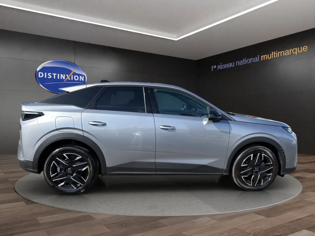 Vue de profil côté droit d’un Peugeot 3008 gris clair avec jantes noires et toit panoramique en showroom.
