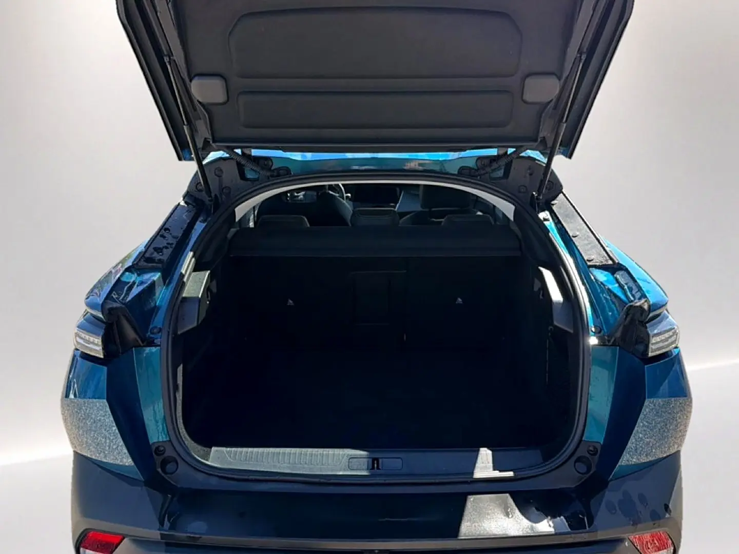 Coffre ouvert vu de l'arrière d'une Peugeot 408 Hybrid 145 allure e-dcs6 bleu, montrant l'espace de chargement vide.
