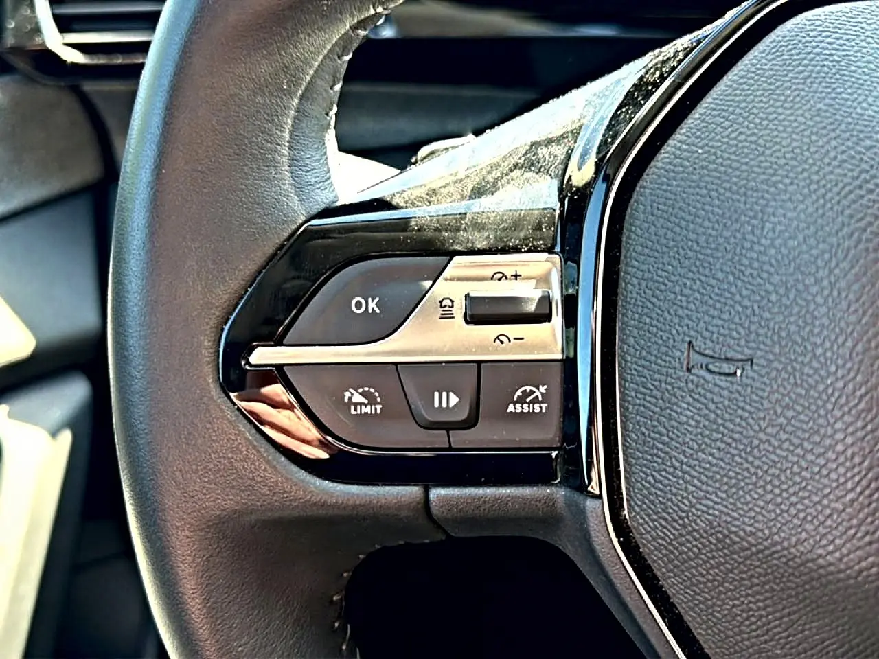 Gros plan sur les commandes multifonctions gauche du volant cuir noir du Peugeot 408 Hybrid 145 allure 2025.