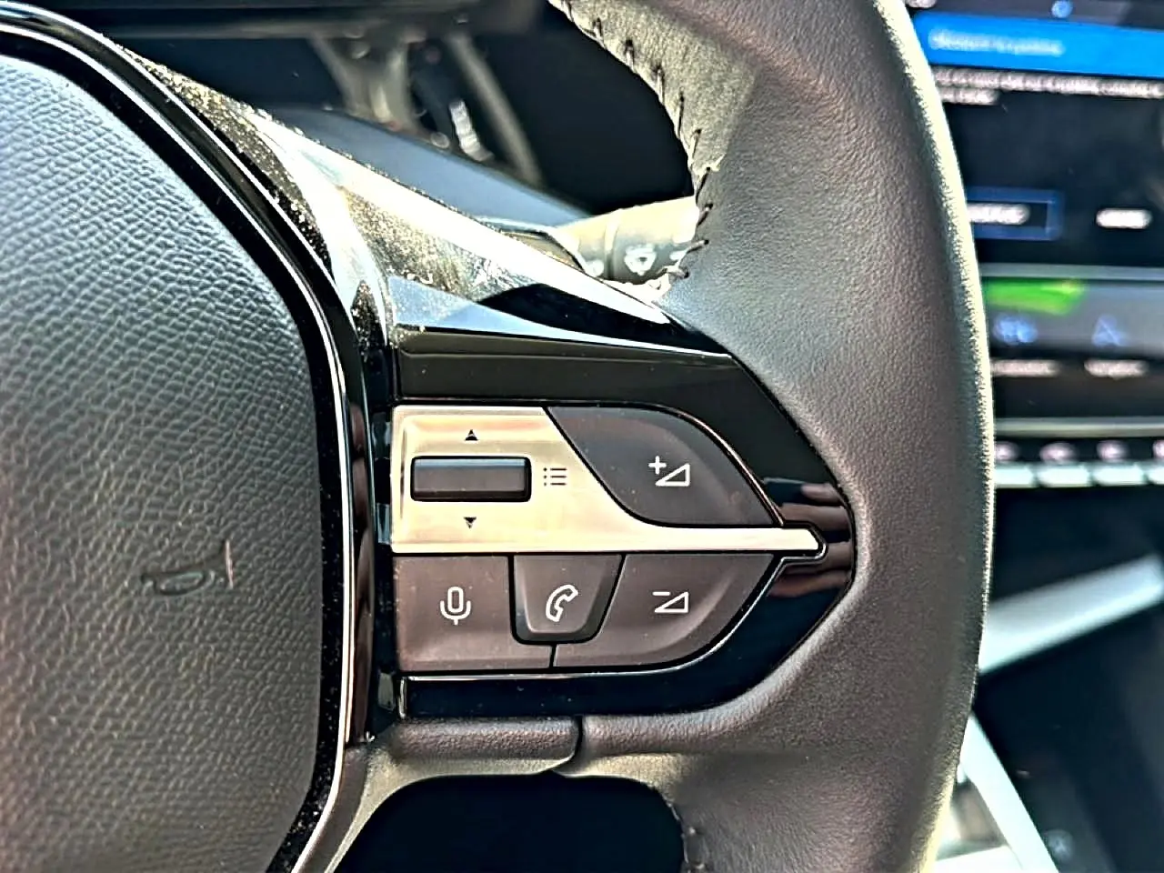 Gros plan sur les commandes du volant cuir noir de la Peugeot 408 Hybrid 145 allure e-dcs6, avec boutons multifonctions.