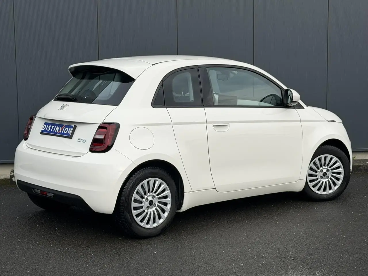 Vue 3/4 arrière droite d'une Fiat 500 électrique blanche 2024 avec porte arrière 3+1 distinctive et jantes multibranches.