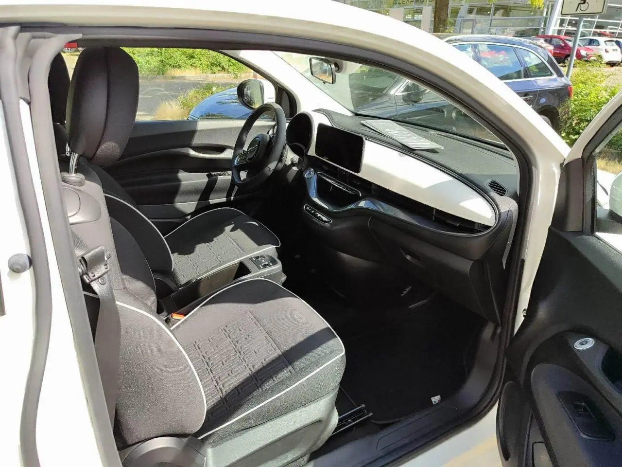 Intérieur de la Fiat 500 électrique blanche vue côté conducteur, montrant sièges noirs et tableau de bord moderne.