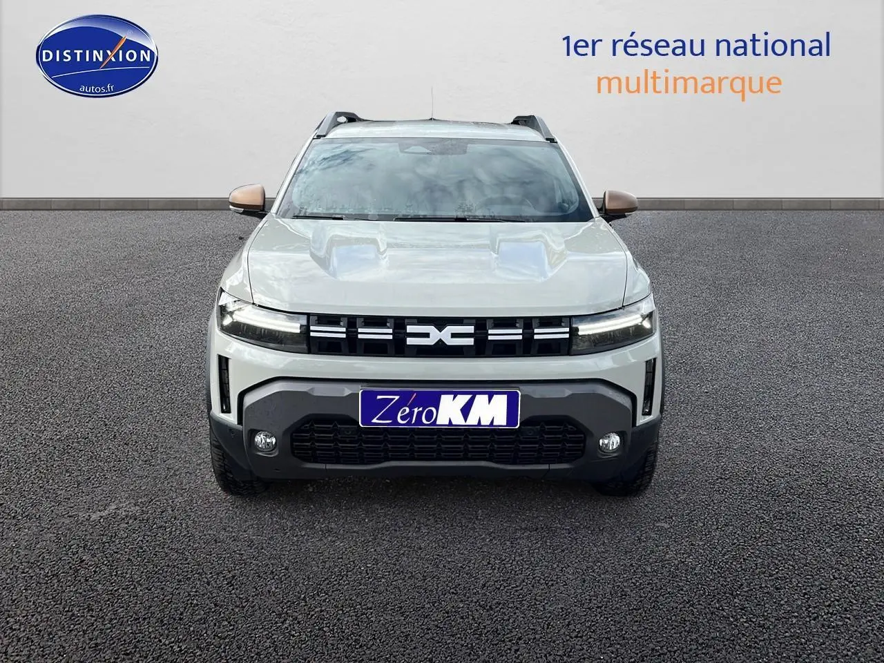 Vue frontale du Dacia Duster 2025 couleur Sandstone avec calandre noire et plaques Zero KM visible.