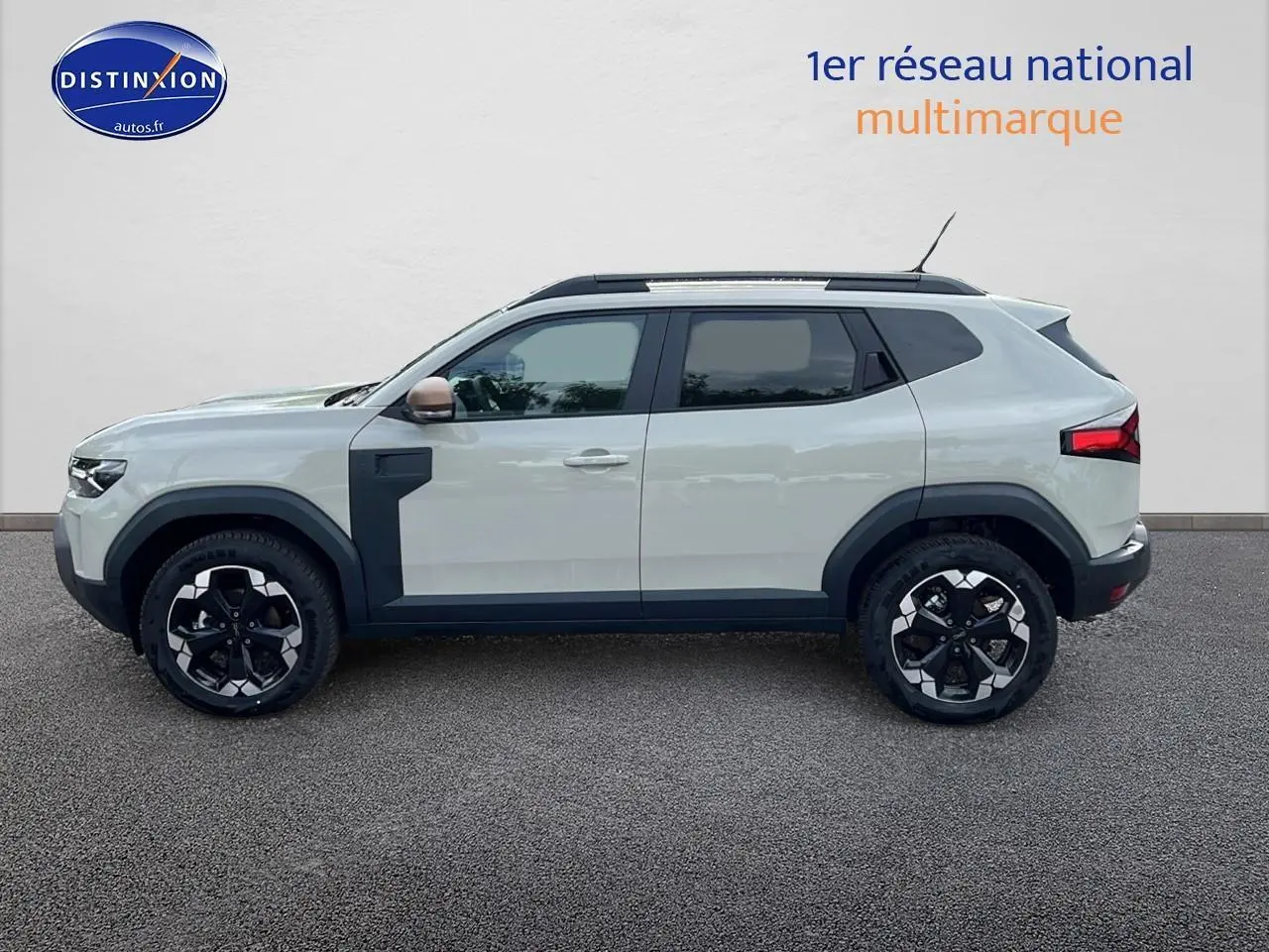 Vue latérale gauche du Dacia Duster 2025 couleur Sandstone avec jantes alu et barres de toit noires.