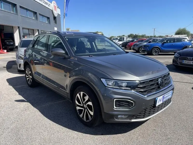 Volkswagen T-Roc 1.5 TSI 150 Active DSG7 gris foncé métal vu en 3/4 avant droit sur parking extérieur.