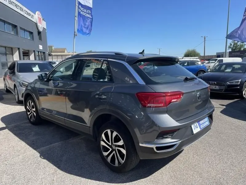 Volkswagen T-Roc gris foncé métal vu en 3/4 arrière droit, avec jantes alliage et toit noir, stationné en extérieur.