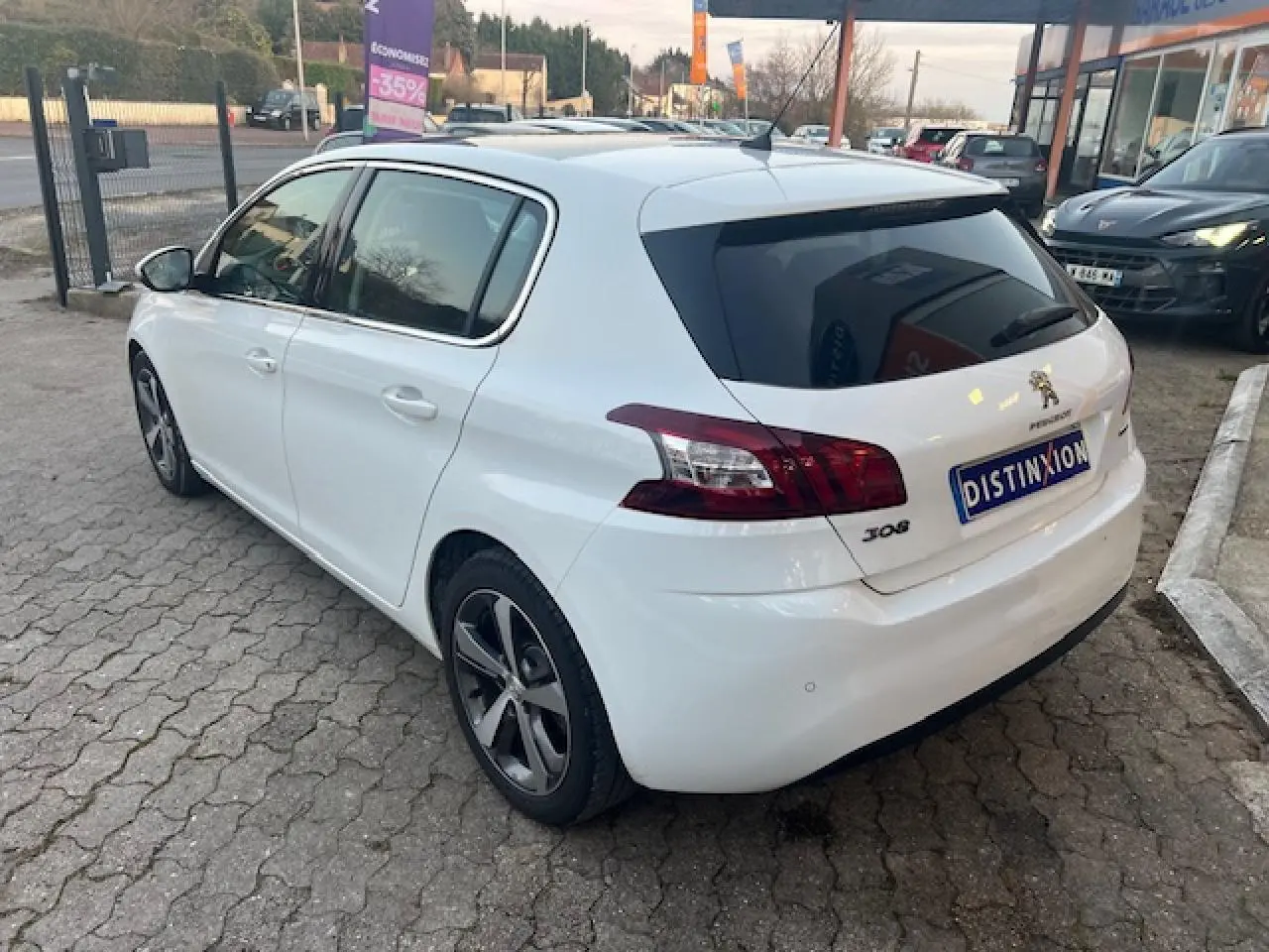 Peugeot 308 blanche vue 3/4 arrière côté gauche, avec toit panoramique et jantes alliage distinctives.