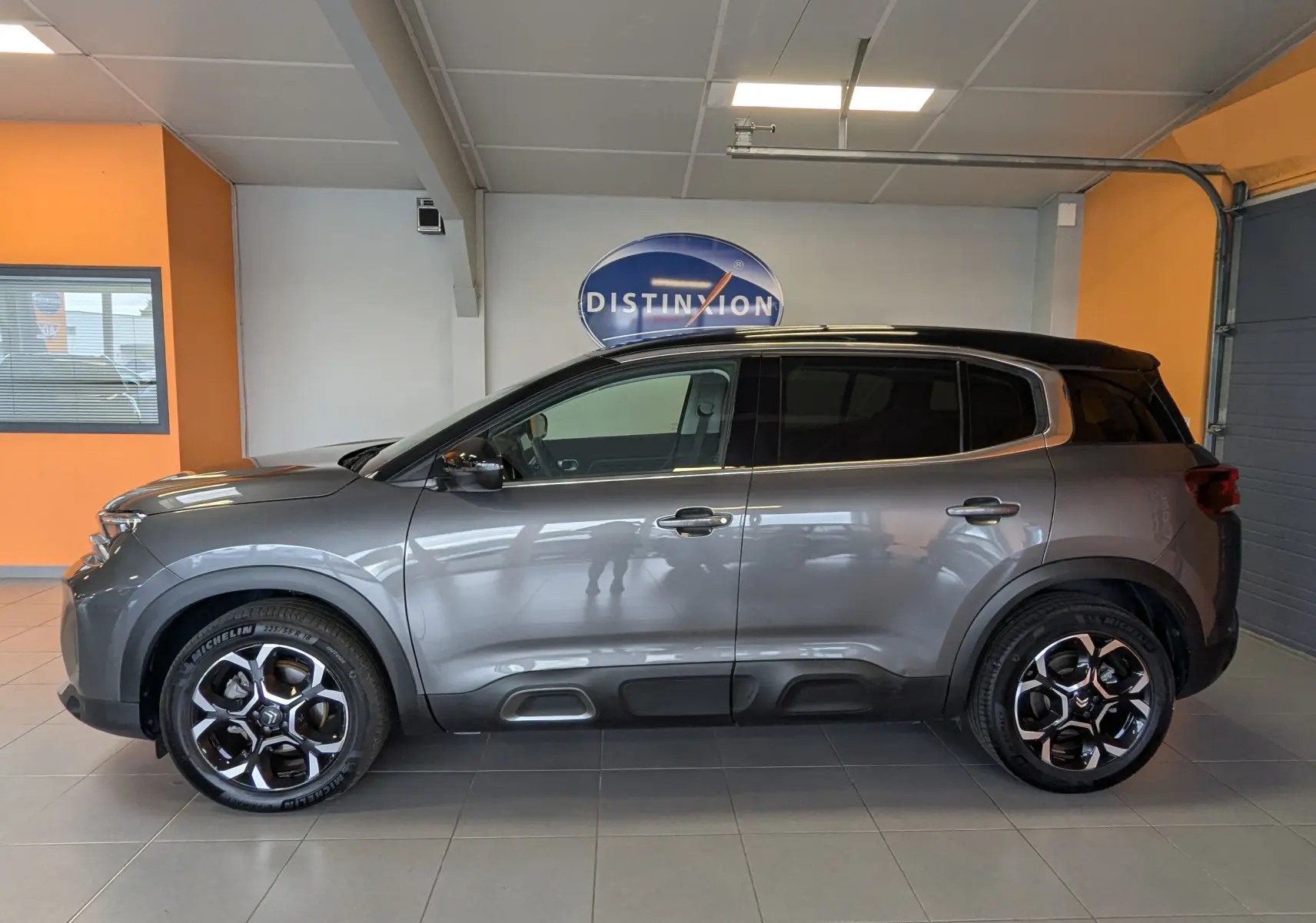 Profil côté gauche du Citroën C5 Aircross hybride gris platinium avec jantes alliage 18 pouces en intérieur showroom.