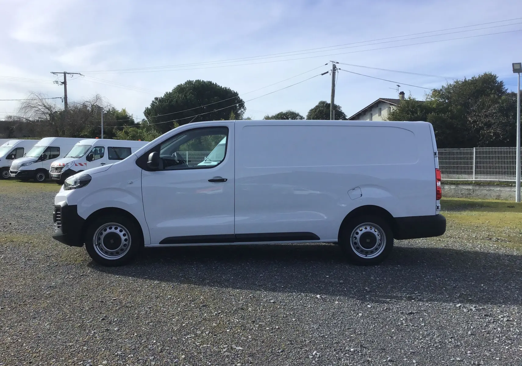 Vue de profil côté gauche d’un FIAT Scudo Fourgon blanc 2024, version XL avec garde au sol réhaussée et protections noires.