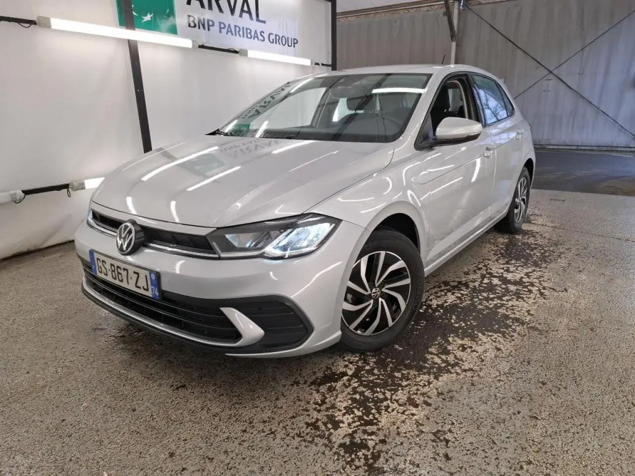 Volkswagen Polo gris clair vue 3/4 avant droit, phares LED allumés et jantes alliage distinctives.