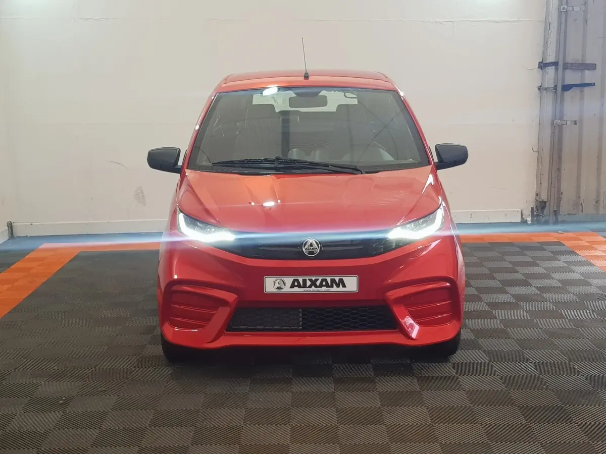 Vue frontale d'une Aixam Ambition 0.5 City Pack rouge avec phares allumés et rétroviseur caméra côté gauche.