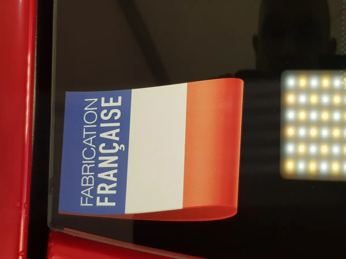 Gros plan sur l'autocollant tricolore "Fabrication Française" sur la carrosserie rouge d'une Aixam Ambition 0.5 City Pack.