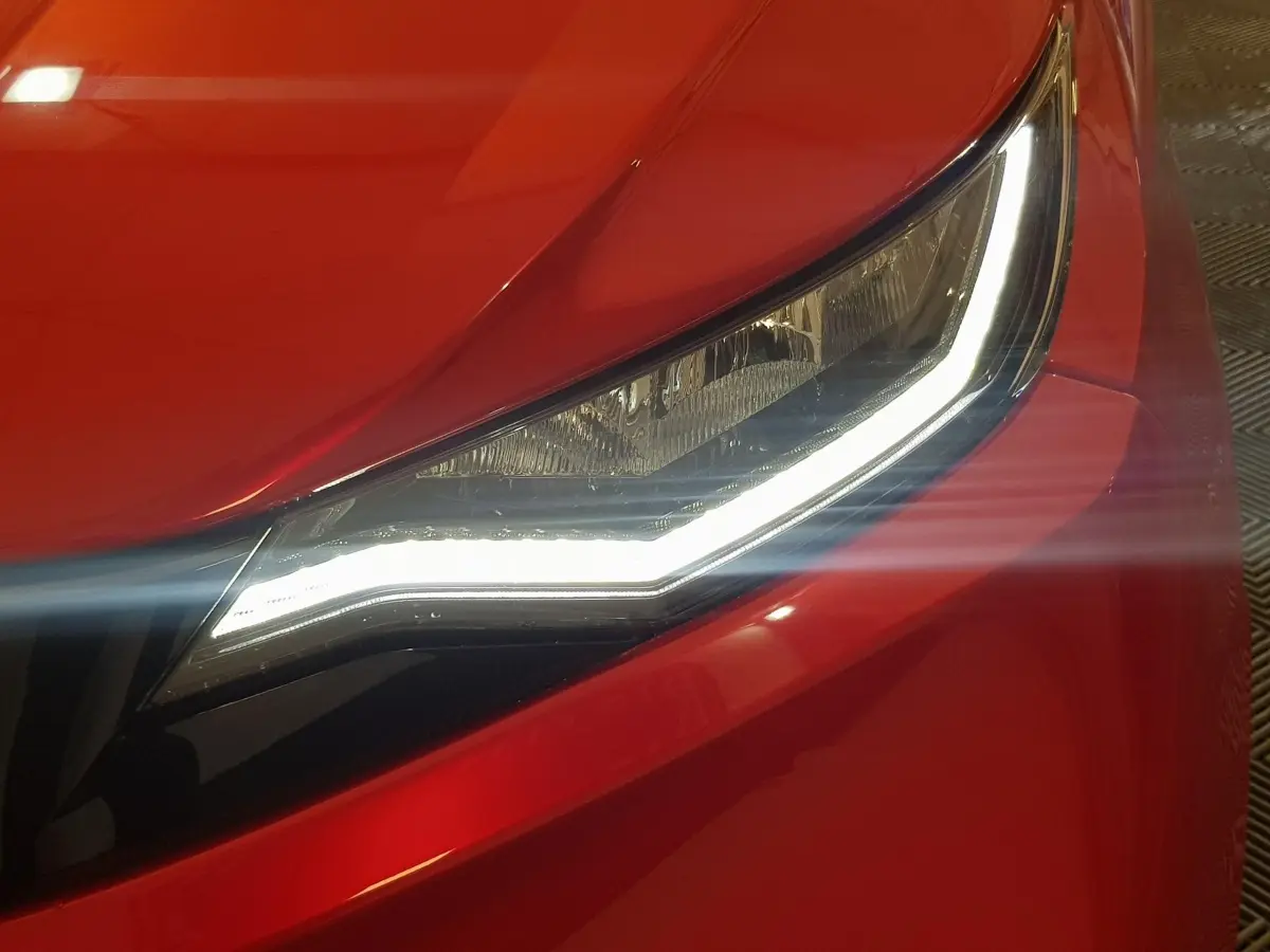 Gros plan sur le phare avant droit allumé d'une Aixam Ambition 0.5 City Pack rouge de 2026.