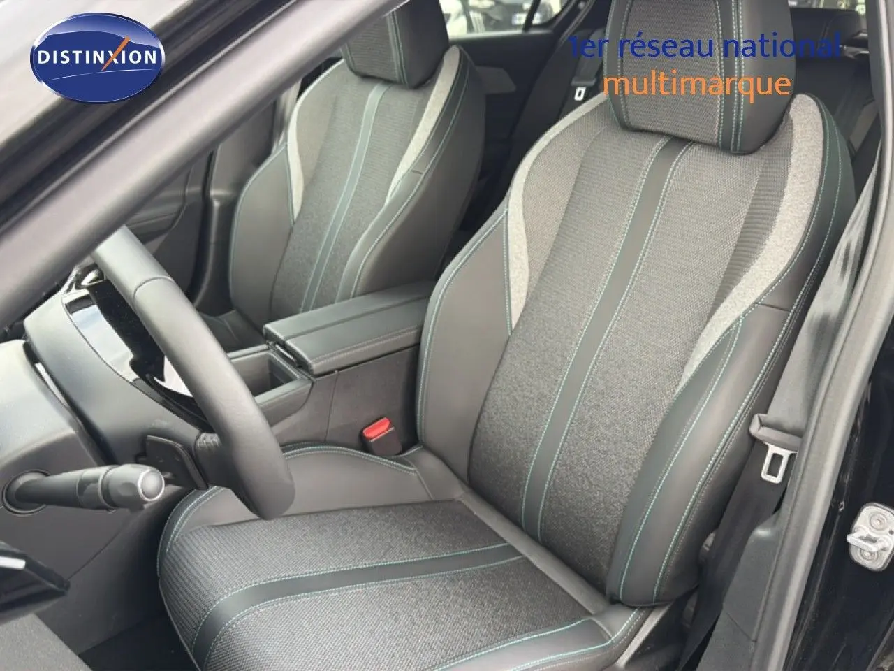 Vue intérieure côté conducteur de la Peugeot 308 1.2 Hybrid 2025, sièges tissu et cuir noir avec surpiqûres bleues.