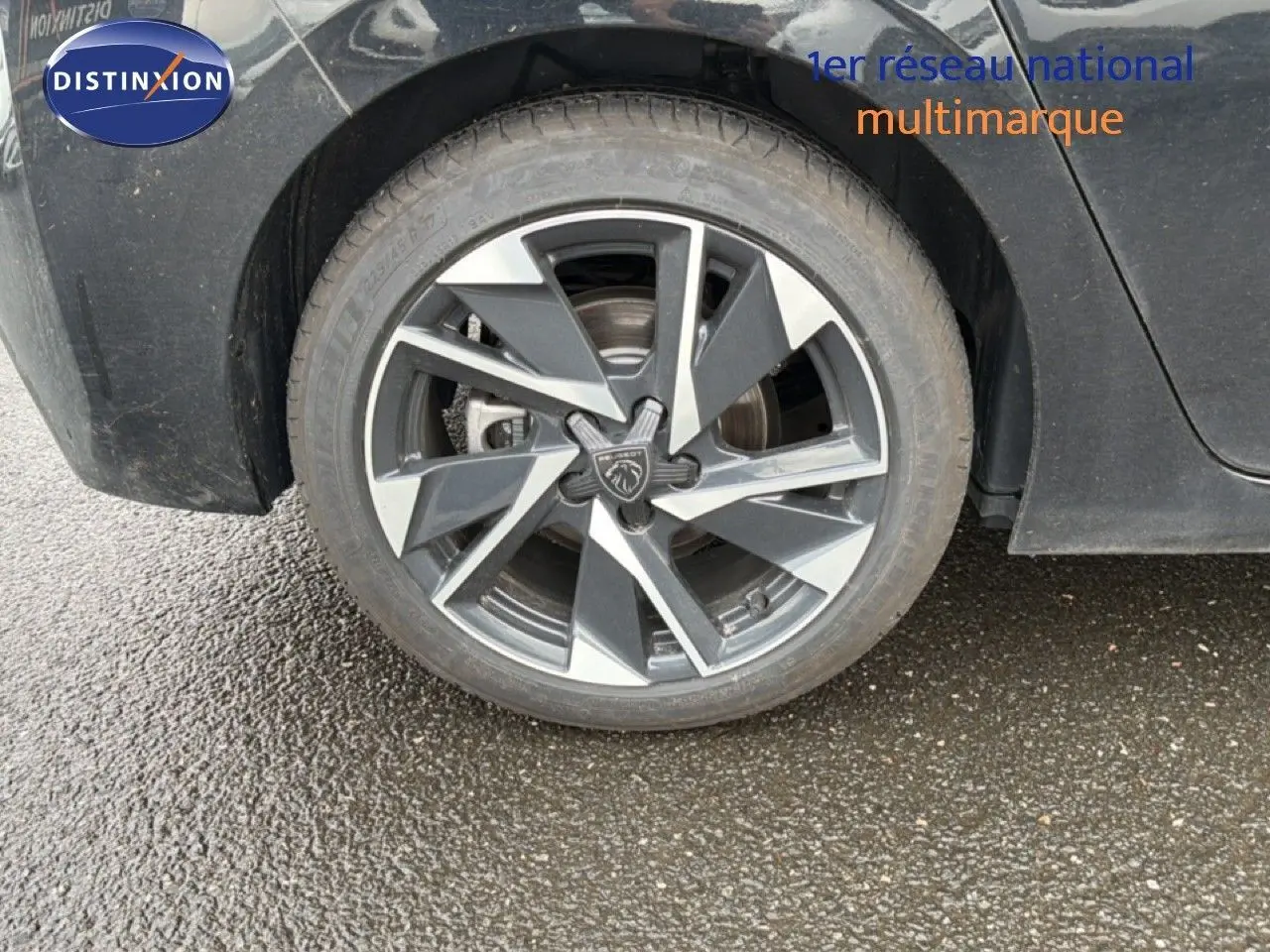 Gros plan sur la roue avant gauche d'une Peugeot 308 noire métal avec jante alliage au design moderne.