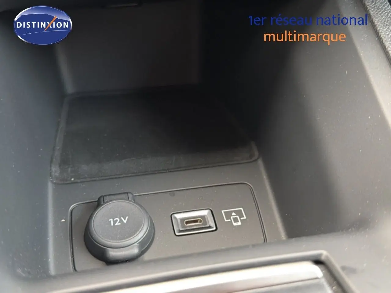 Gros plan sur la prise 12V et port USB dans le compartiment central d'une Peugeot 308 noire hybride 2025.