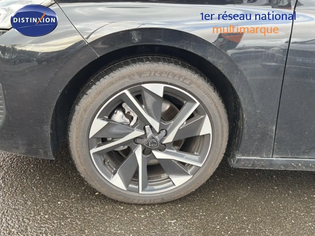 Gros plan sur la roue avant gauche d'une Peugeot 308 noire métal, mettant en valeur la jante alliage au design moderne.