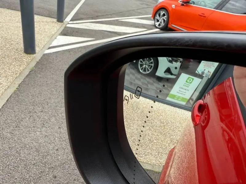 Vue latérale droite en miroir du rétroviseur, montrant la portière rouge flamme d'un Renault Austral 2025 hybride.
