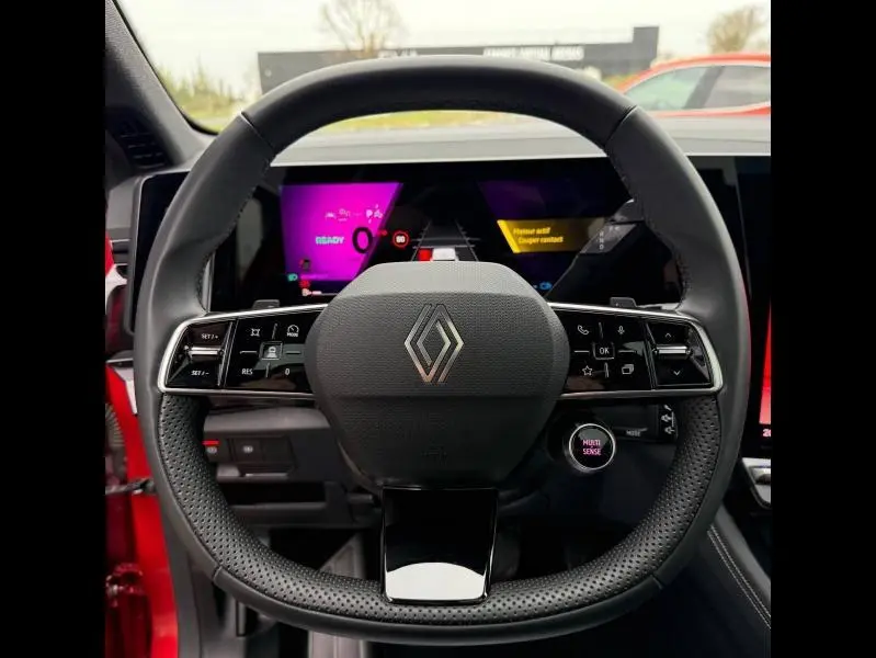 Vue frontale du volant perforé noir du Renault Austral 2025 Rouge Flamme, avec tableau de bord numérique coloré en arrière-plan.