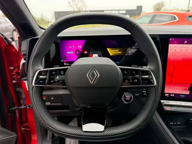 Vue centrée sur le volant du Renault Austral rouge flamme 2025, avec tableau de bord numérique et écran tactile visible.