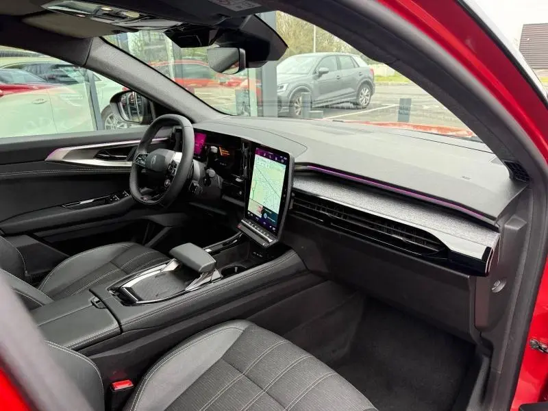 Vue intérieure côté conducteur du Renault Austral rouge flamme 2025, avec écran tactile vertical et tableau de bord moderne.