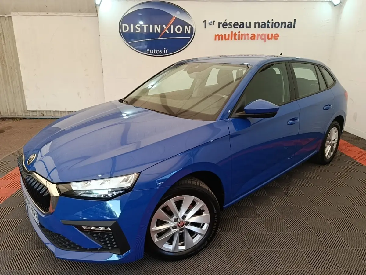 SKODA SCALA 1.5 TSI bleu vue 3/4 avant droit, jantes alliage et calandre chromée visible en intérieur showroom.