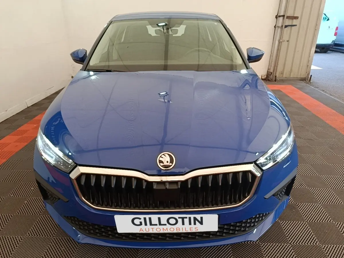 Vue avant d'une Skoda Scala 1.5 TSI bleu, avec calandre noire et phares LED allumés dans un garage.