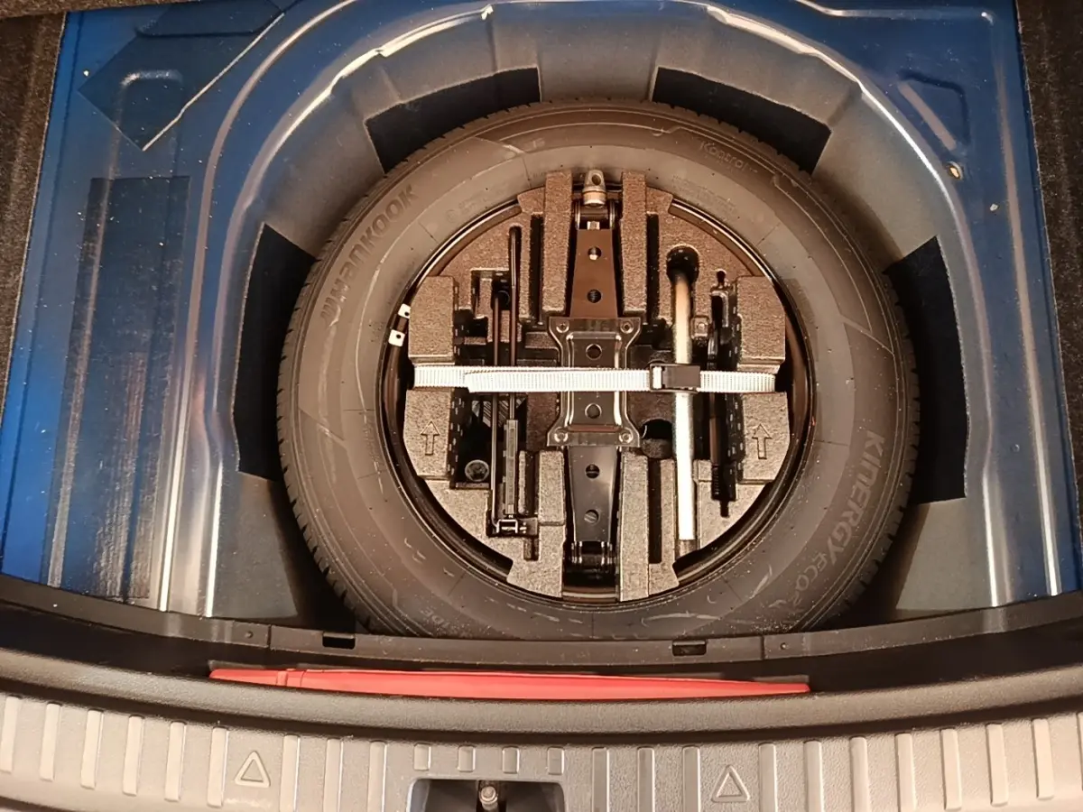 Vue plongeante sur la roue de secours galette et outils dans le coffre d'une Skoda Scala bleu 2024.