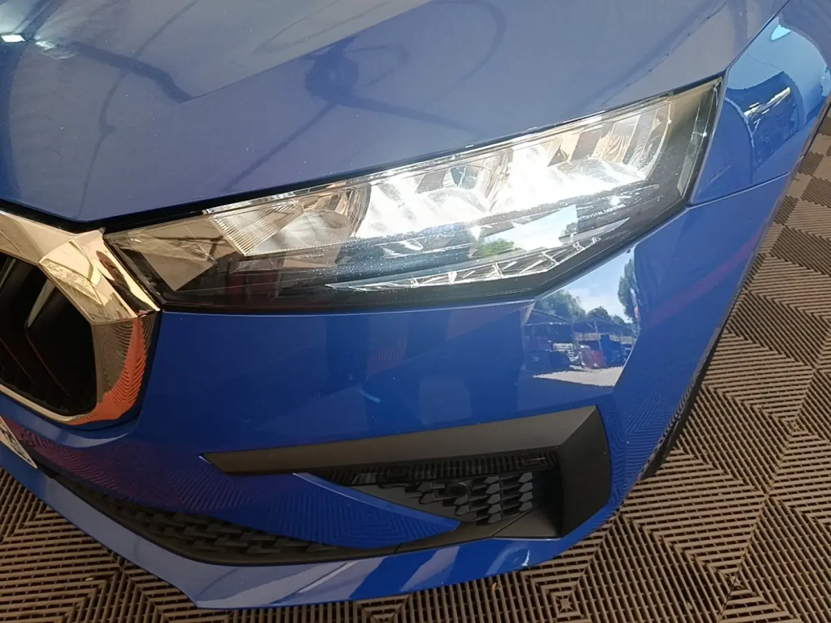 Gros plan sur l'avant droit bleu d'une Skoda Scala 2024, mettant en valeur le phare LED et la calandre chromée.