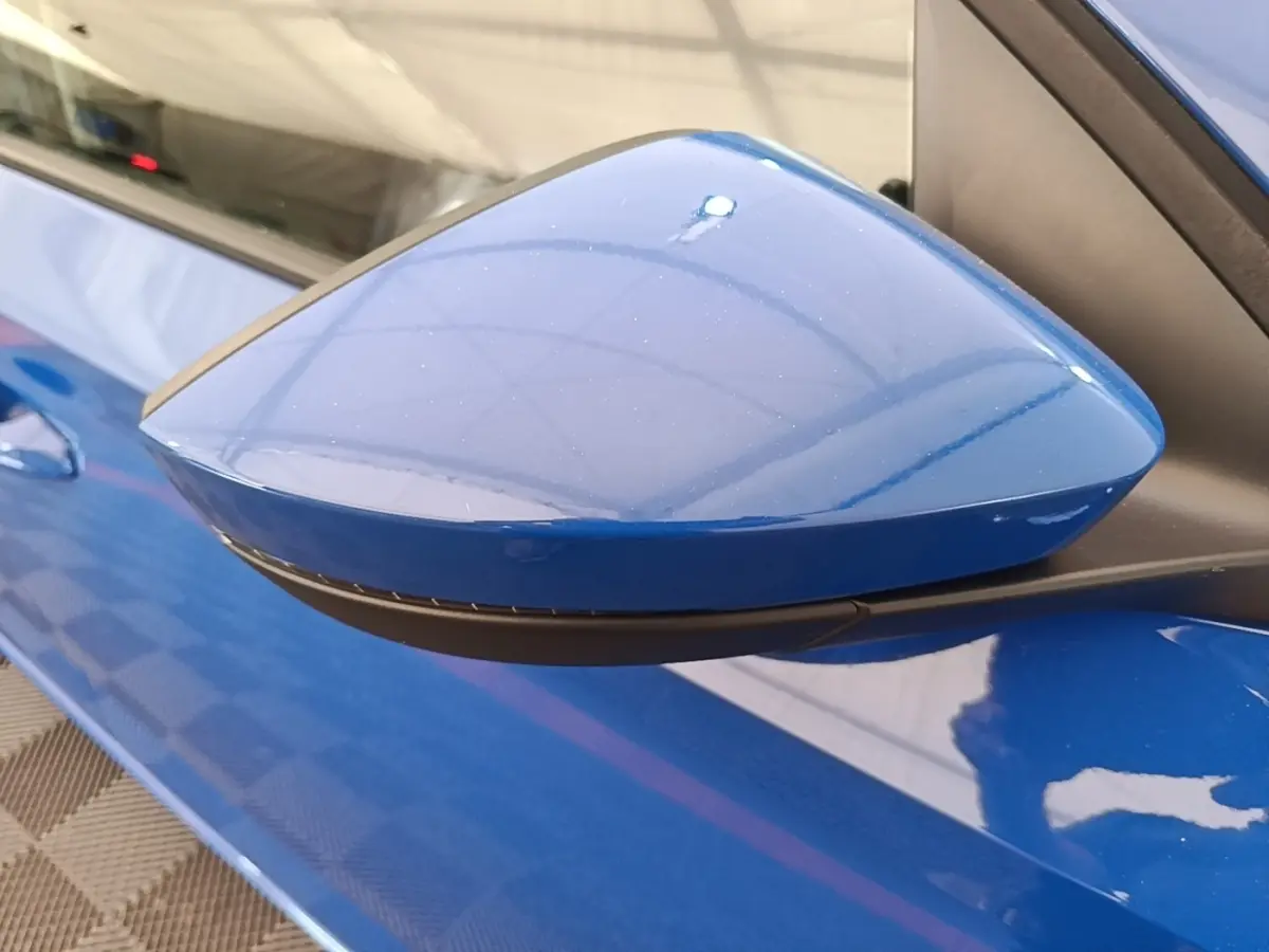 Rétroviseur côté gauche bleu métallisé de la SKODA SCALA 1.5 TSI 2024, avec carrosserie et poignée assorties visibles.
