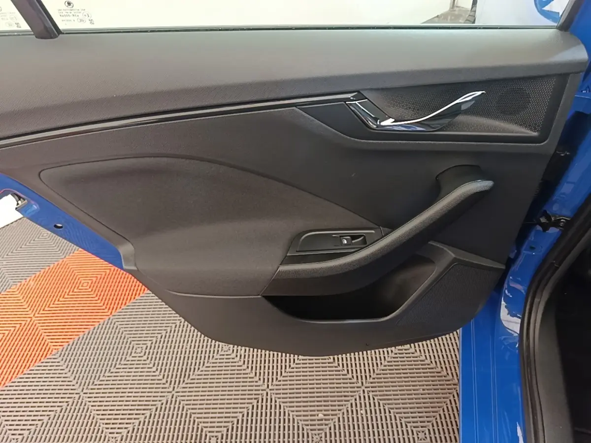 Gros plan sur la porte avant gauche bleue d'une Skoda Scala 2024, avec poignée chromée et commande de vitre intégrée.