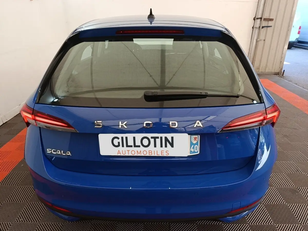 Vue arrière d'une Skoda Scala bleue 2024 avec feux LED et logo SKODA bien visibles sur un sol à damier noir et orange.
