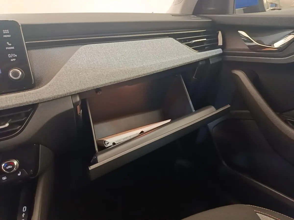 Intérieur de la Skoda Scala 2024, vue côté passager sur la boîte à gants ouverte avec tableau de bord gris et noir.