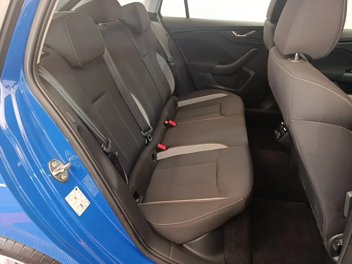Vue intérieure côté gauche sur la banquette arrière noire avec surpiqûres et portière bleu vif ouverte d’une Skoda Scala 2024.