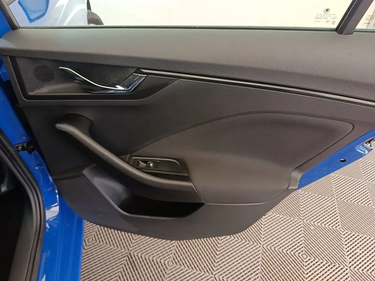 Vue intérieure côté gauche de la porte avant d'une Skoda Scala 2024 bleue avec poignée chromée et bouton de lève-vitre.