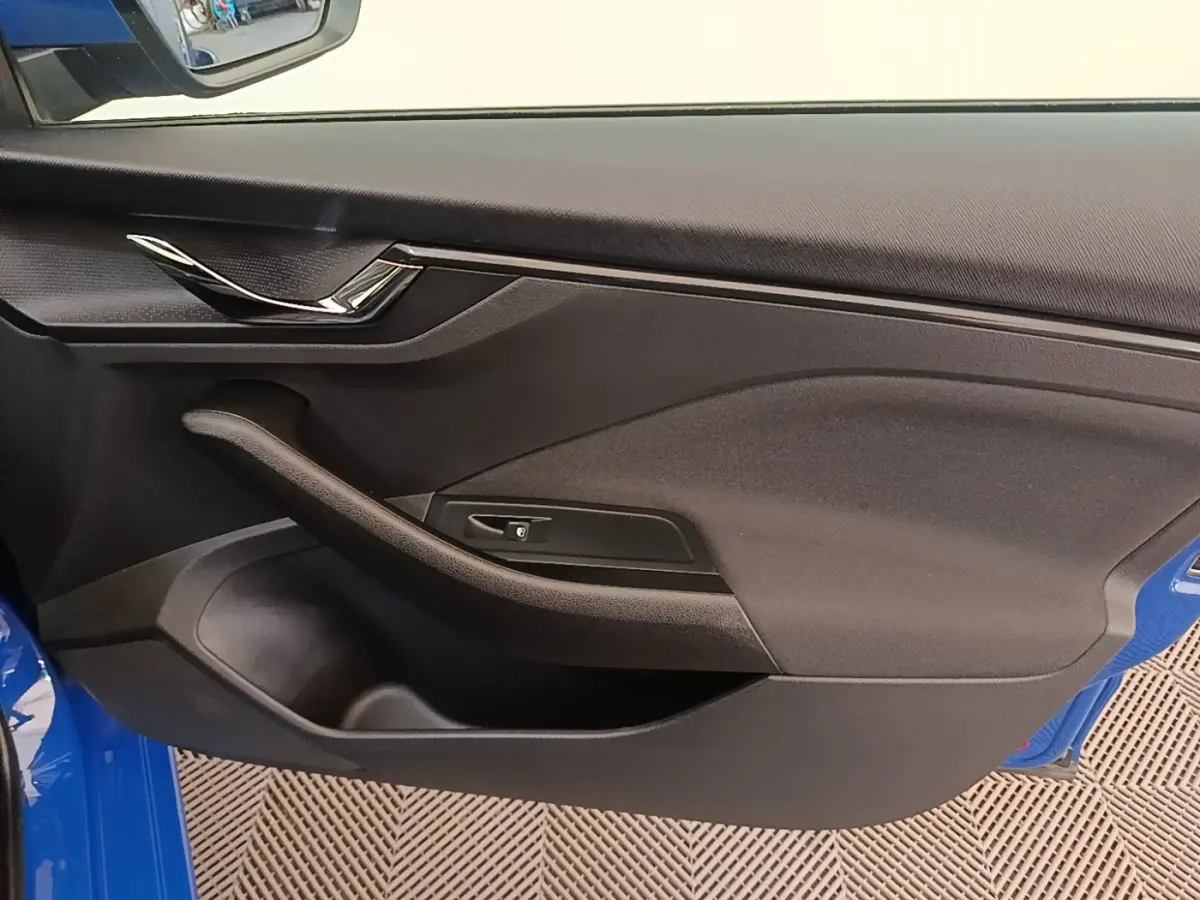 Vue intérieure de la porte avant gauche d’une Skoda Scala 2024 bleu, avec poignée chromée et accoudoir noir.