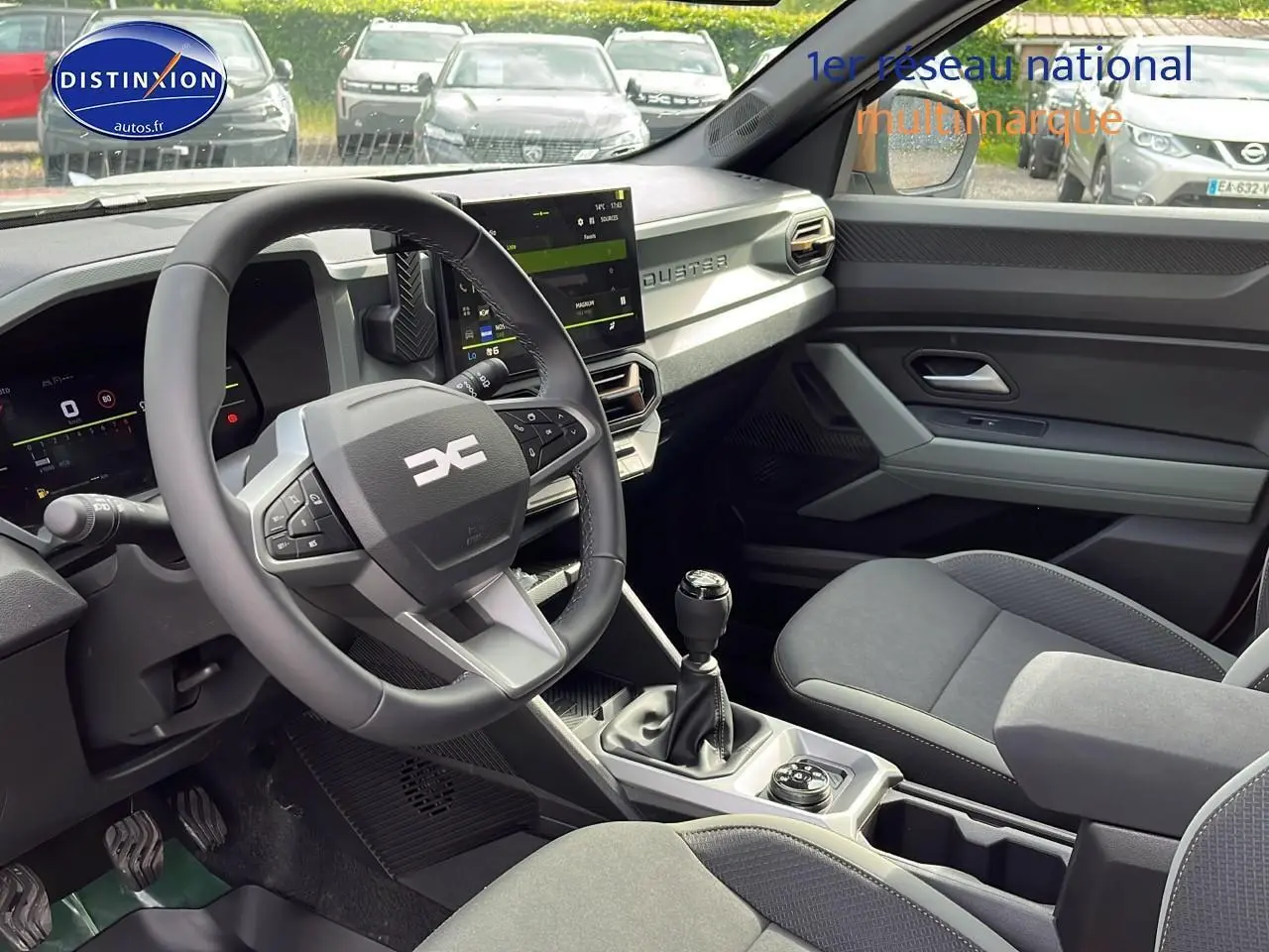 Intérieur avant du Dacia Duster 2025 avec volant multifonction, écran tactile et sellerie grise.