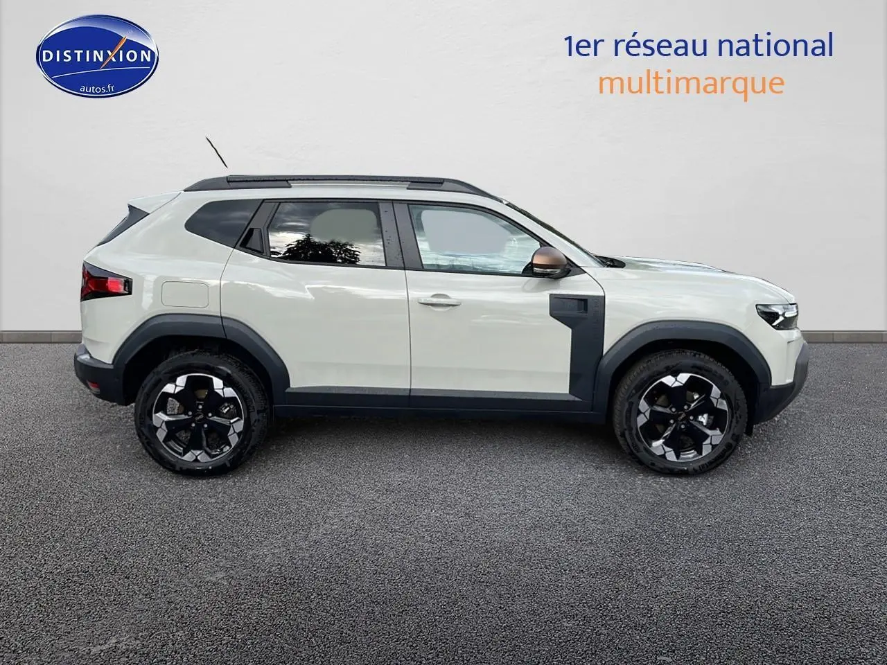 Profil côté gauche du Dacia Duster 2025 couleur Sandstone avec jantes alu et barres de toit noires.