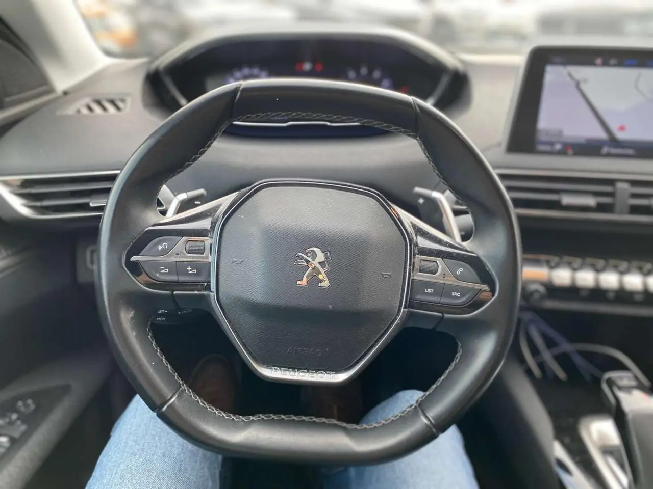 Vue intérieure centrée sur le volant cuir du Peugeot 3008 noir, avec tableau de bord et écran de navigation visibles.