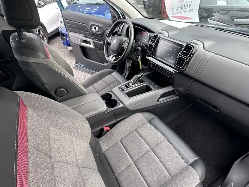 Vue intérieure côté conducteur du Citroën C5 Aircross Bleu Tijuca 2021, avec tableau de bord et sièges gris à surpiqûres rouges.