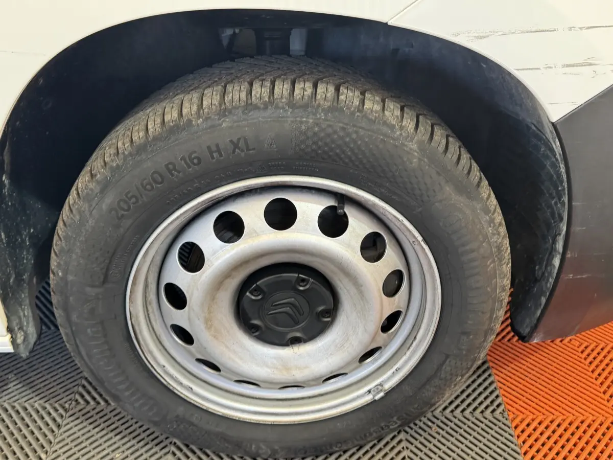 Gros plan sur la roue avant droite d’un Citroën Berlingo blanc avec jante acier et logo Citroën au centre.