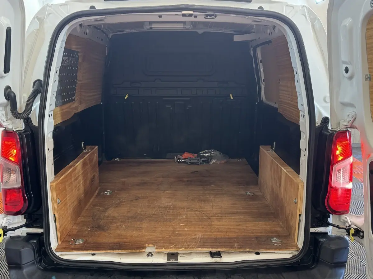 Vue arrière ouverte du Citroën Berlingo blanc 2020 montrant l'espace de chargement en bois et les feux arrière allumés.