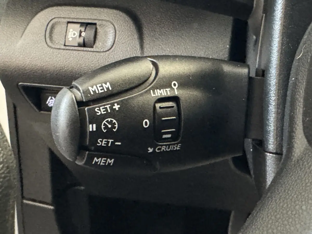 Gros plan sur la commande de régulateur de vitesse noire à gauche du volant du Citroën Berlingo blanc, intérieur.