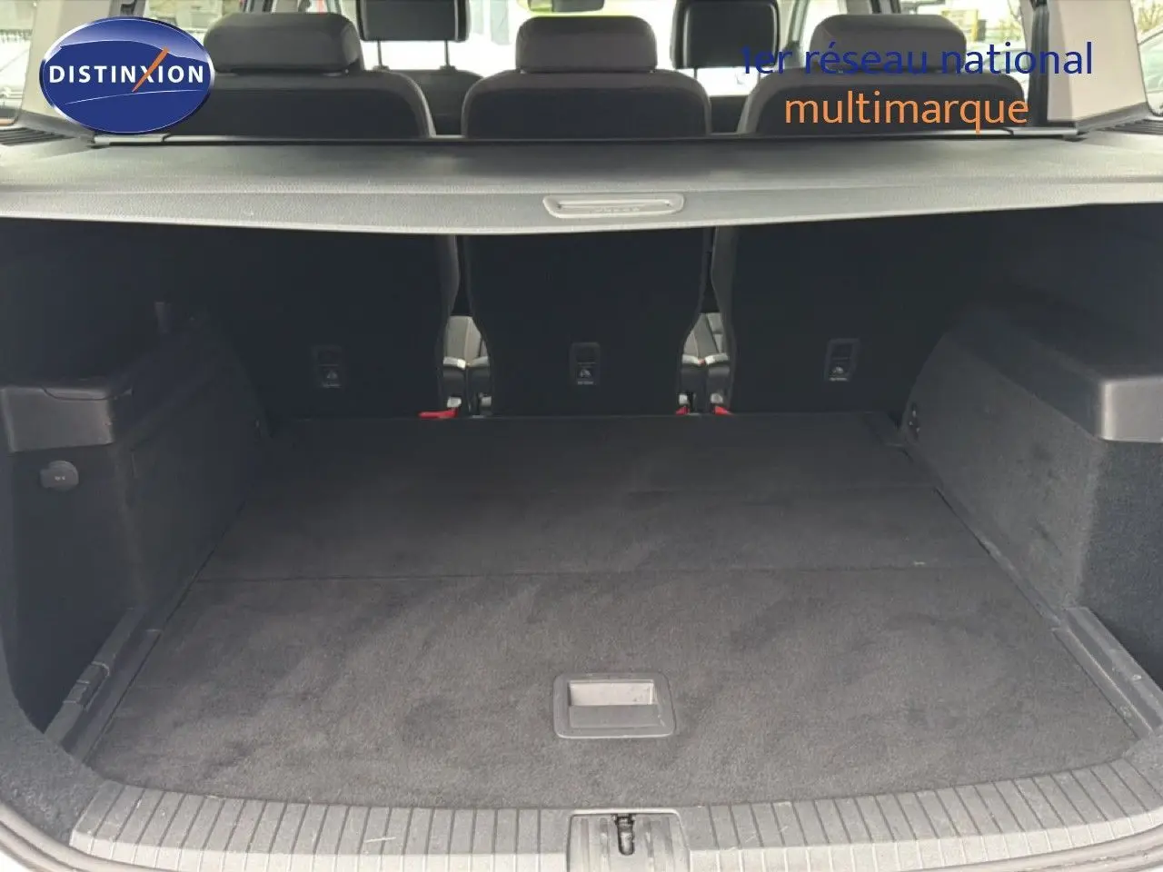 Coffre spacieux du Volkswagen Touran blanc 2018 vu de l'arrière avec banquette arrière rabattue et cache-bagages.