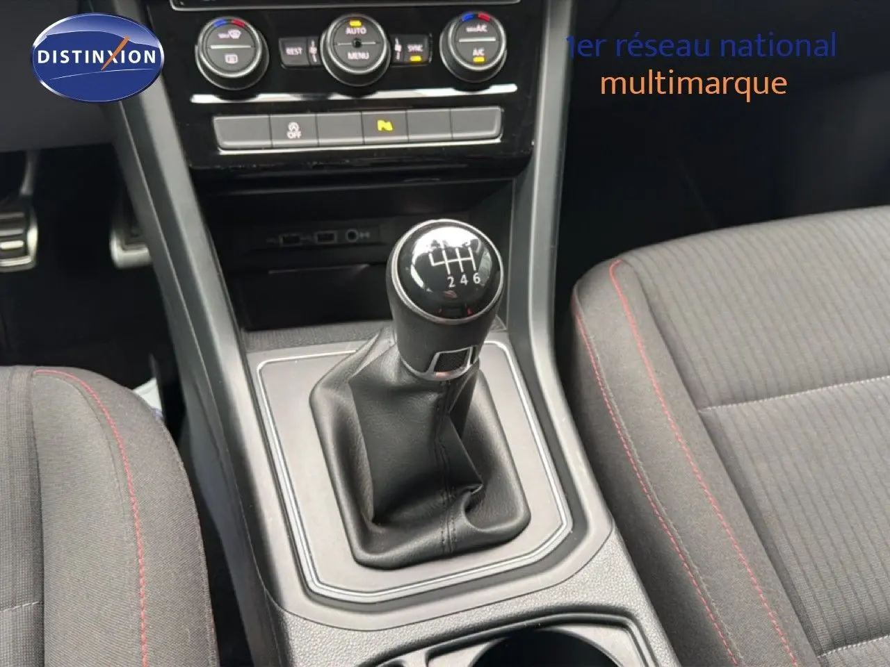 Gros plan sur le levier de vitesses manuel noir et la console centrale du Volkswagen Touran 2018, avec sièges tissu gris à surpiqûres rouges.