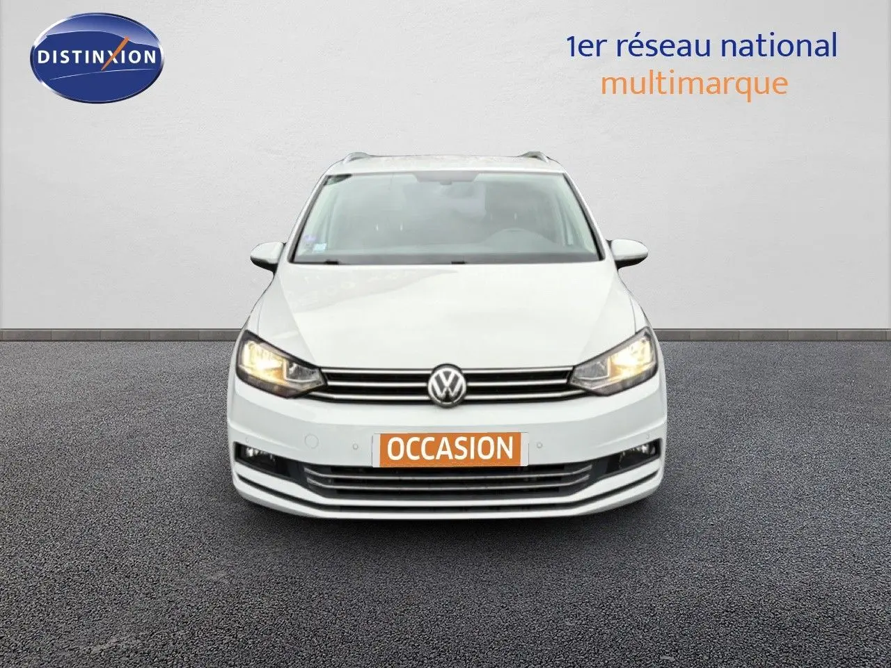 Vue avant d’un Volkswagen Touran blanc de 2018 avec phares allumés et plaque « OCCASION » visible.