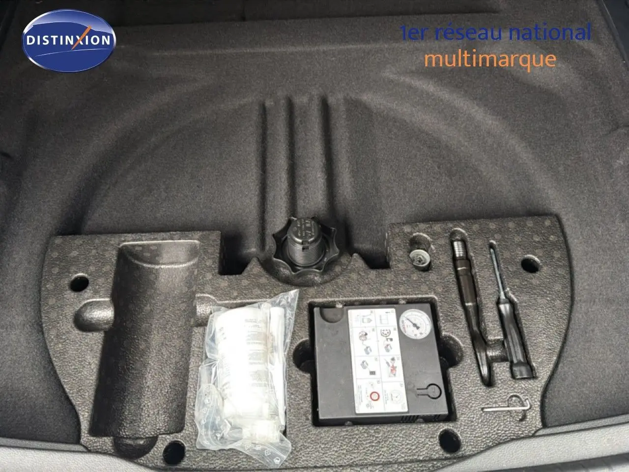 Vue rapprochée du coffre d’un Volkswagen Touran blanc 2018 montrant le kit de réparation pneu et outils intégrés.